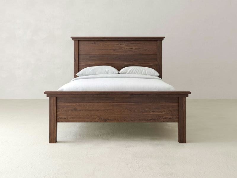 The Ivy Bed - Tobacco by James+James stands against a plain, light-colored background, neatly made with white pillows and a light-colored duvet. This wooden frame bed with its headboard features a simple and rustic design.