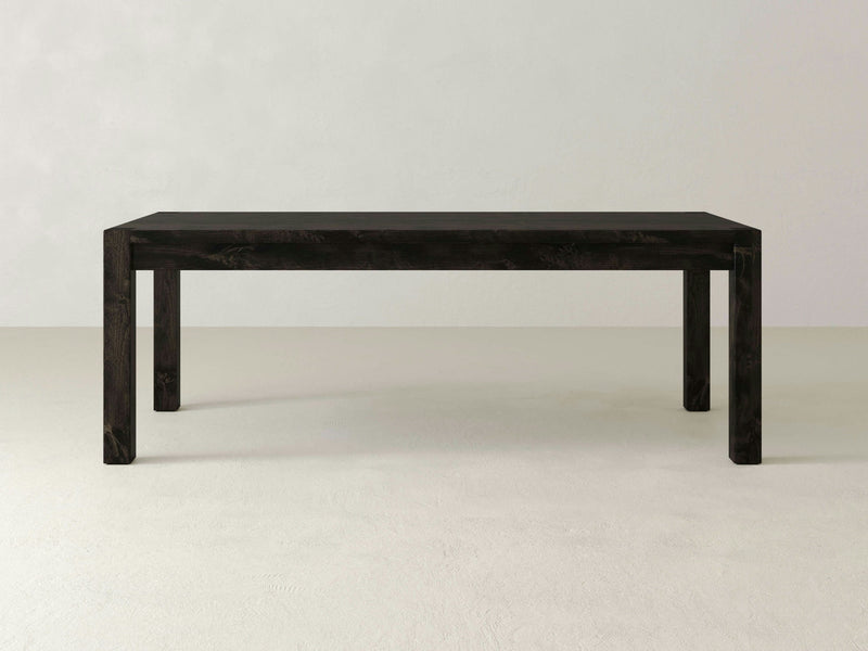 The Jonathan Dining Table - Charred Ember from James+James is a minimalist, rectangular dark wood table with straight legs. Positioned against a plain, light-colored background, its design exudes simplicity and modernity with clean lines and a uniform dark finish.