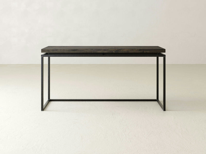 A minimalist, rectangular console table by James+James, known as the Floating Top Sofa Table - Deep Grey, stands against a plain, light-colored background. The design is simple and contemporary, featuring a dark wooden top and sleek black metal legs with clean lines and angles.