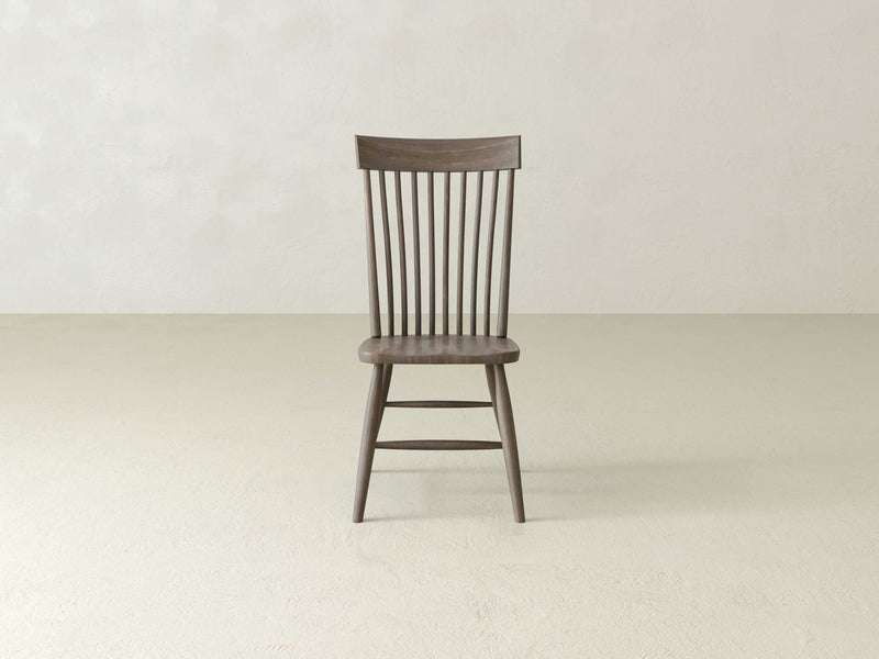 The Eleanor Side Dining Chair from James+James is centered in a minimalistic, empty room with light-colored walls and flooring. This single chair, made of barn wood with a dark stain, features vertical slats on the backrest and boasts a simple, classic design.