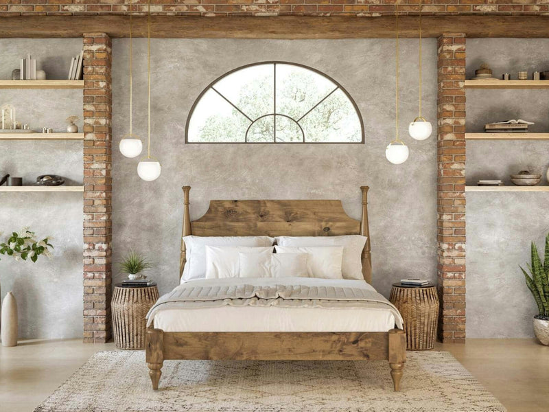 A cozy bedroom features the Stella Bed in Harvest Wheat from James+James, adorned with white bedding against a textured gray wall. A large arched window above the bed lets in natural light. The brick accents, plants, and hanging pendant lights add warmth and charm to the room.