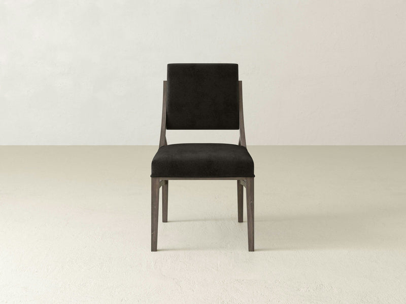 A straight-on view of the Quinn Dining Chair by James+James showcasing its minimalist design with a black cushioned seat and backrest. The chair features sleek, dark wooden legs and frame, set against a plain, light-colored background—perfect for elegant gatherings in your dining room decor.