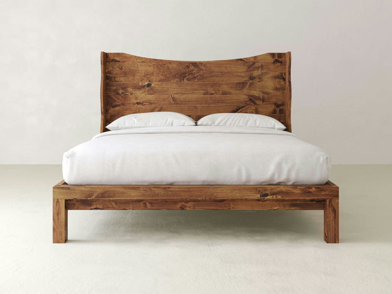 The Harlow Bed - Tuscany by James+James, with its rustic, handcrafted appearance, stands against a plain white wall. The bed is made up with a white fitted sheet, a white comforter, and two white pillows, creating a simple and minimalistic look.