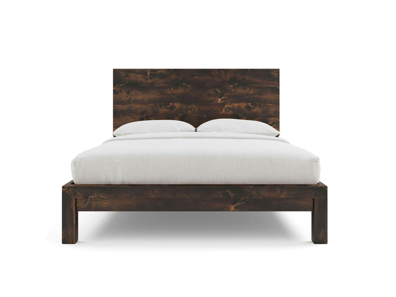 A Sawyer Bed in a rich tobacco finish from James+James is displayed. The bed, featuring a simple and minimalist wooden frame, is dressed with a white comforter and two neatly arranged white pillows against the headboard. The image highlights the bed's clean lines and modern design.