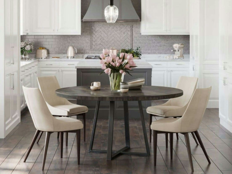 A modern kitchen with white cabinets and a gray backsplash features the Watson Round Dining Table in deep grey from James+James, accompanied by four beige chairs. A centerpiece of pink tulips in a vase sits on the table. The kitchen also includes stainless steel appliances and a pendant light hanging above.