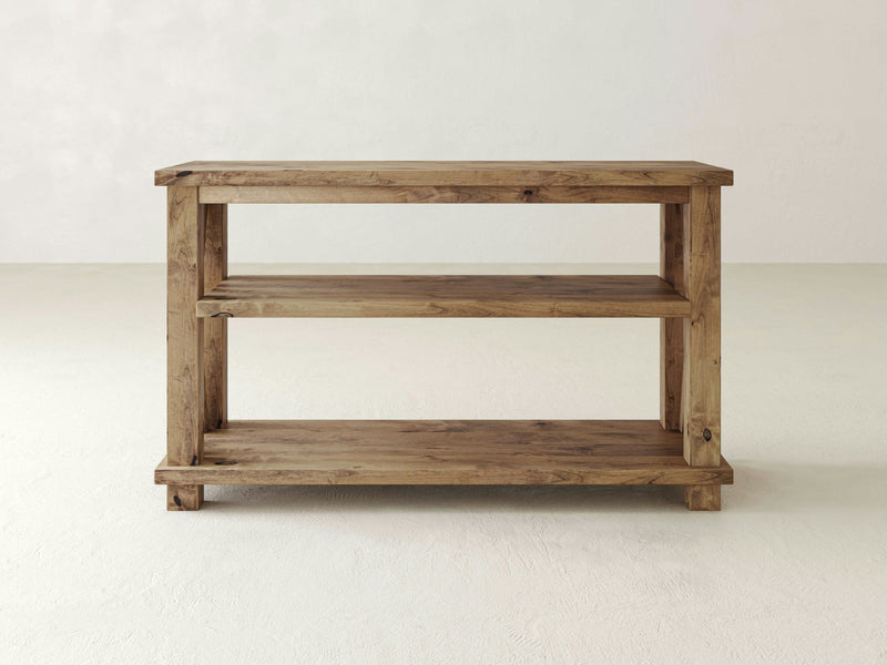 The Carter X Sofa Table - Harvest Wheat from James+James is a wooden two-tier console table with a simple, rustic design. This table features open shelving with a natural finish, highlighting the wood grain. It stands on a light-colored floor against a plain, off-white background.