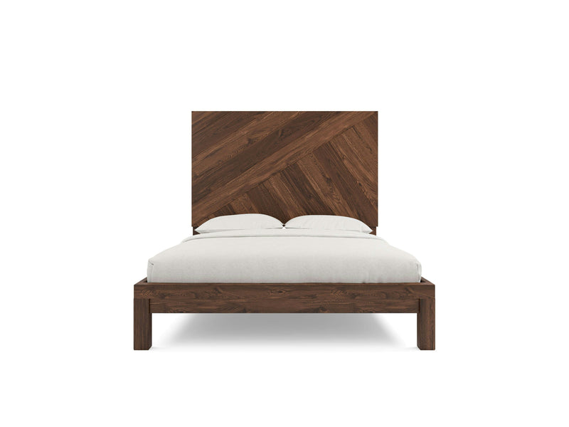 Front view of the Luna - Tobacco wooden bed by James+James, showcasing a high headboard adorned with diagonal planks in a herringbone pattern. The bed is elegantly dressed with white bedding, including pillows and a blanket, and rests on a simple geometric frame.