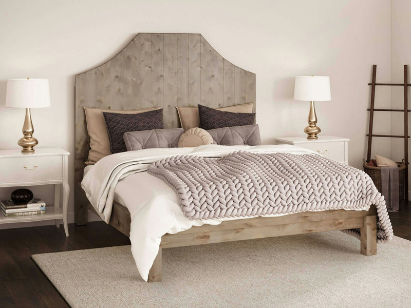 A cozy bedroom features the Megan Bed - Barn Wood by James+James, adorned with pillows and a chunky knit blanket. Two matching white nightstands with gold lamps flank the bed. A ladder-style rack and neutral decor complete the serene setting.