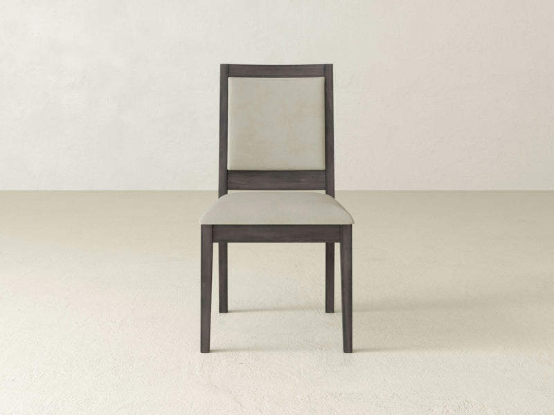 Introducing the Gina Side Dining Chair - Deep Grey by James+James. This elegant wooden chair features a straight backrest, and is finished in a sophisticated deep grey color. Both the backrest and seat are cushioned and upholstered in a luxurious light beige fabric, creating a striking contrast. The chair is showcased against a plain off-white background for added emphasis.