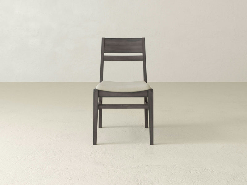 A single Delilah Dining Chair - Deep Grey by James+James with a lightly cushioned white seat is centered in an empty, minimalist room with a plain, light-colored background. The chair features a simple, modern design with horizontal slats on the backrest.