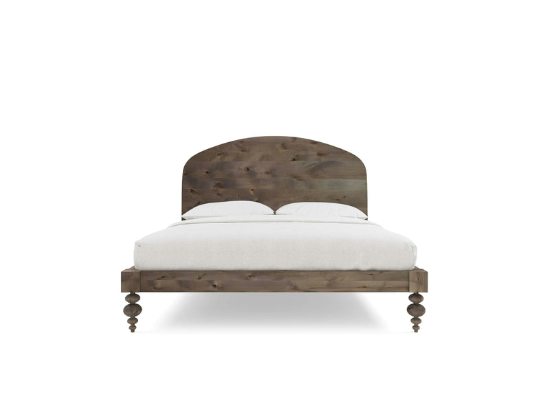 The Eden Bed - Barn Wood by James+James is displayed from the front view, showcasing an arched headboard and turned legs. Made from wooden material with a rustic finish, it is adorned with white bedding and two pillows, epitomizing a simple and traditional style.