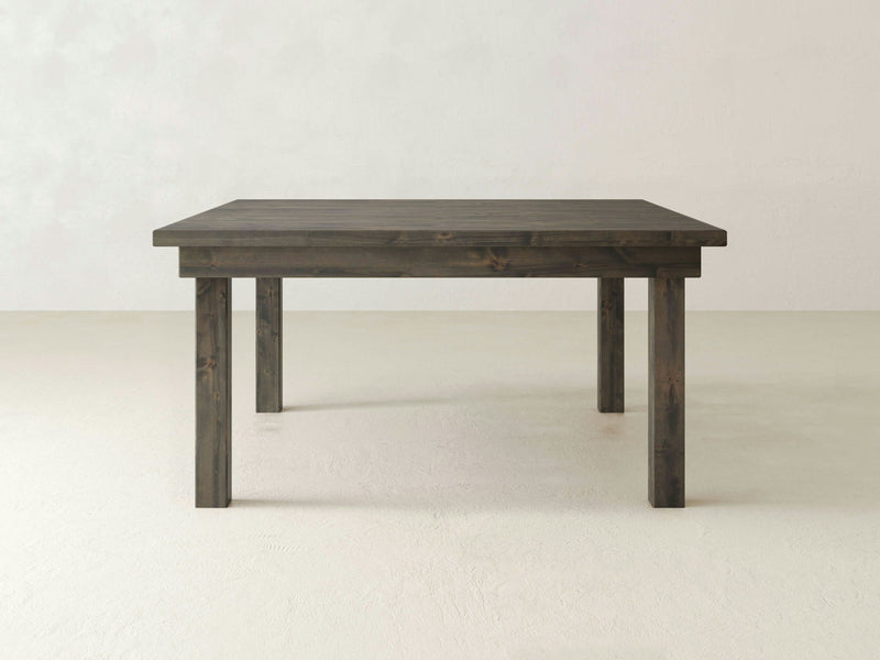 The Farmhouse Square Dining Table - Deep Grey by James+James is set against a plain white background. This dark wooden table boasts a simple rectangular design with a minimalist and rustic look, featuring four sturdy legs and a flat, smooth surface.