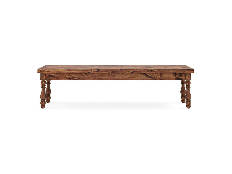 The Annli Bench - Tuscany by James+James is a wooden rectangular bench with a rustic finish, featuring four ornate, turned legs. The bench has a simple, elegant design with a slightly distressed look, making it suitable for dining or as a decorative accent piece in a home.