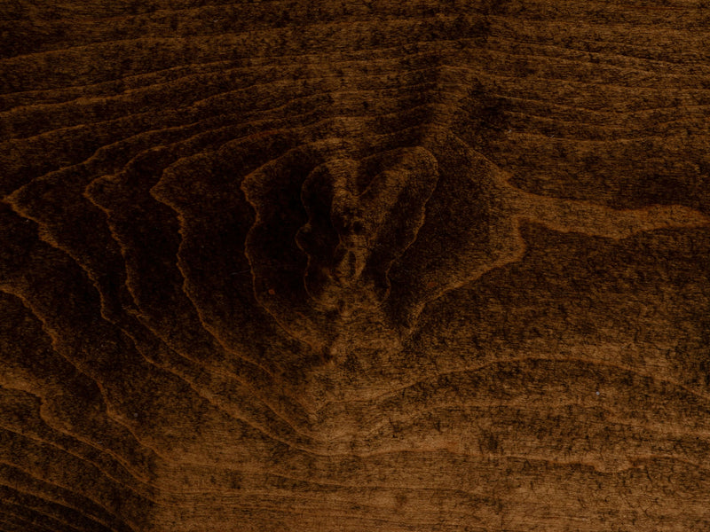 Close-up image of the Tobacco on Maple Sample by James+James, showcasing textured dark brown wood with prominent grain patterns and subtle variations in shade. The grain lines create a wavy, natural design, highlighting the rich color and intricate details of the wooden surface.