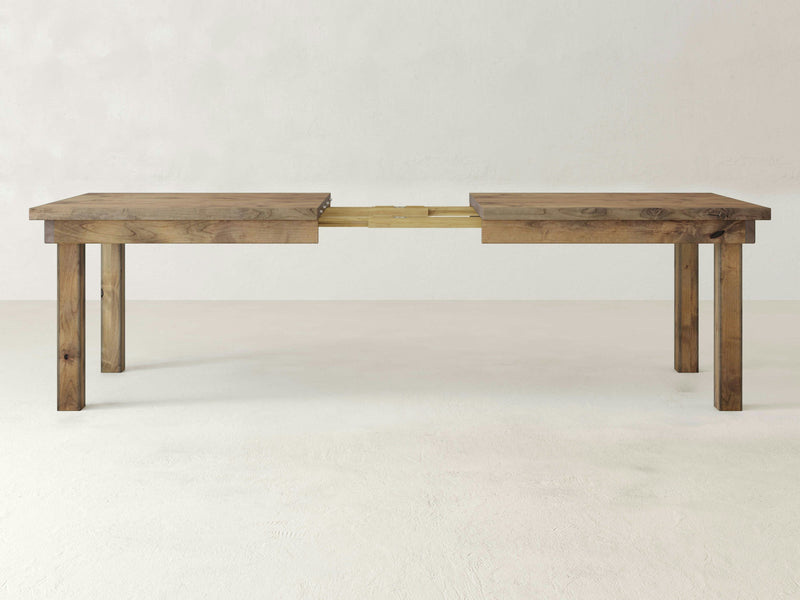 The Farmhouse Expandable Dining Table - Harvest Wheat by James+James features a light brown finish and is partially extended, displaying the separated end sections with the middle section in view. It stands on four rectangular legs and is showcased in a minimalist setting.