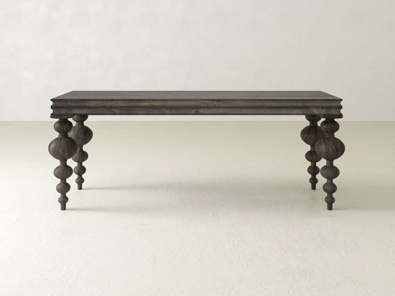 An Olivia Sofa Table in deep grey from James+James sits on a plain, light-colored floor. The table features intricately carved, bulbous legs with multiple rounded segments, combining rustic and elegant design elements.