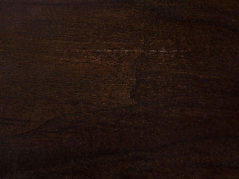 A close-up of the Charred Ember on Black Walnut Sample by James+James showcases a dark brown wooden surface with a smooth texture and visible grain patterns. The lighting accentuates the color variations and natural imperfections of the wood, enhancing its rich, warm tones. The polished finish highlights the depth and character of this elegant wood sample.