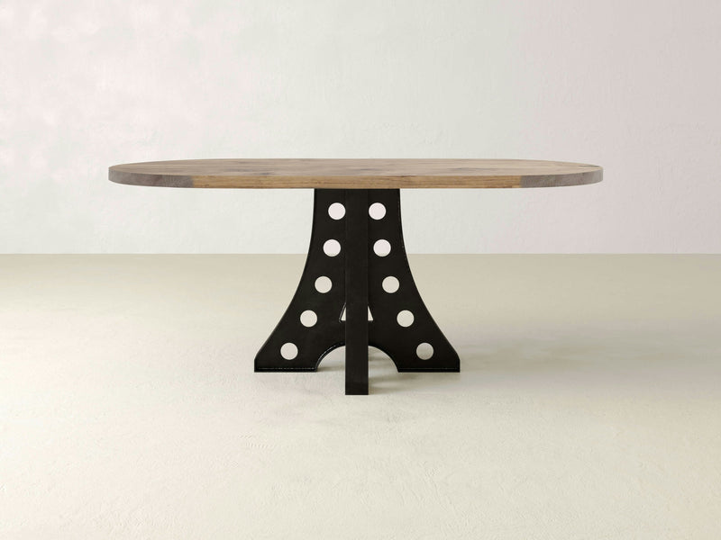 The Amelia Oval Dining Table in Harvest Wheat by James+James showcases a light-toned top and a unique black base with circular cutouts, set against a plain, light-colored background.