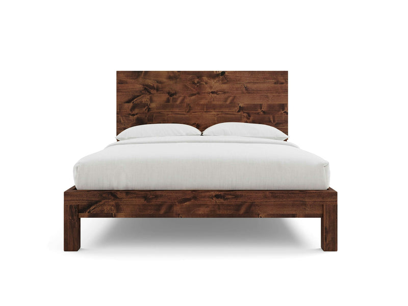 The Sawyer Bed - Tuscany by James+James features a wooden bed frame with a high, rustic headboard crafted from dark-stained wood. The bed is elegantly made with a white duvet and two white pillows. Its minimalist and modern design accentuates the natural wood grain and texture.