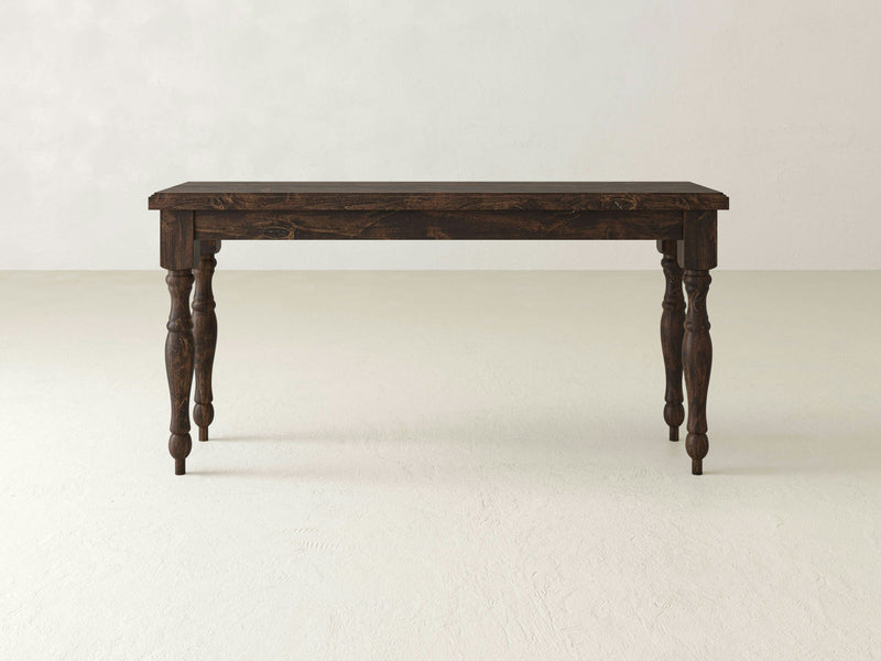 The Abigail Sofa Table by James+James, featuring a dark wooden rectangular top and ornate, carved legs, stands on a light-colored floor against a plain, light-colored wall. The table boasts a rustic appearance with its traditional design in a rich Tobacco finish.