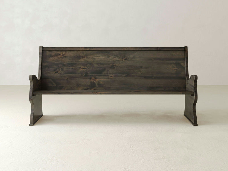 The Rustic Church Pew Bench - Deep Grey by James+James, with its high backrest and curved armrests, sits on a plain, light-colored floor against a neutral wall backdrop. The deep grey wood appears polished with a natural grain pattern visible.