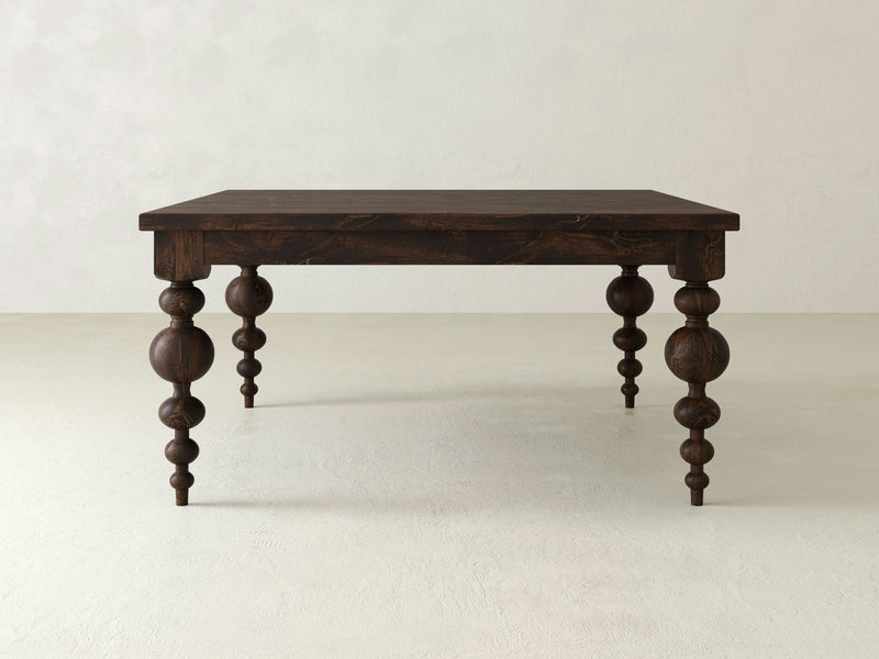 The Olivia Square Dining Table by James+James features a dark wooden design with an artisan-built, square top, and four intricately carved, rounded legs. Set against a light, minimalist backdrop that contrasts beautifully with its deep hue, this table’s exquisite craftsmanship and contemporary elegance are truly highlighted.