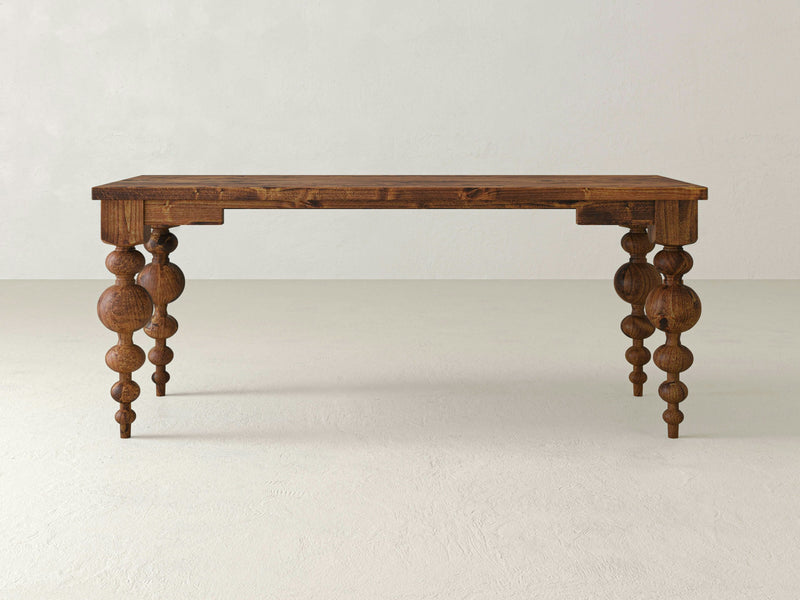 The Olivia Desk - Tuscany by James+James showcases a wooden rectangular top and intricately turned legs with spherical accents. Set against a plain white background, the desk highlights its detailed craftsmanship and rustic design.