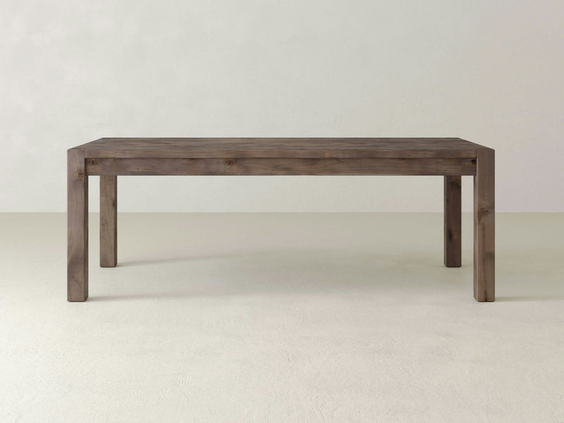 The Jonathan Dining Table - Barn Wood by James+James is a simple, rectangular wooden table with a natural finish. It features straight legs at each corner and boasts a minimalist design that highlights the wood grain and natural texture. The table is set against a plain, light-colored background.