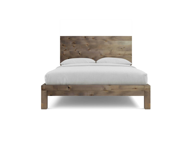 The Sawyer Bed - Barn Wood by James+James is displayed from the front, showcasing its rustic finish. The minimalist bed frame features a tall wooden headboard and is dressed with white linens, including a flat sheet and two pillows. The background remains plain white.