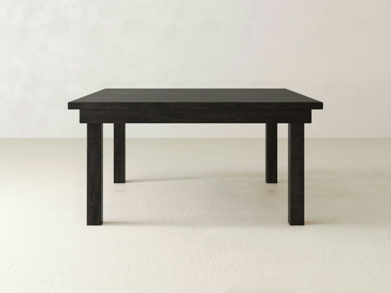 A minimalist, square wooden table in a charred ember finish from James+James, featuring clean lines and a smooth surface, is set against a plain light-colored background. This Farmhouse Square Dining Table has four straight legs and a simple design.