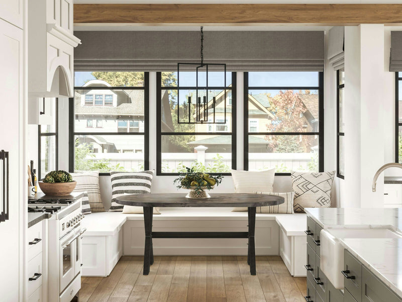 Bright, modern kitchen with a built-in corner bench seating around a James+James X-Base Oval Dining Table in Deep Grey. Large windows let in natural light, highlighting gray cushions and throws. White cabinetry, a farmhouse sink, and a gas stove complete the airy, inviting space.