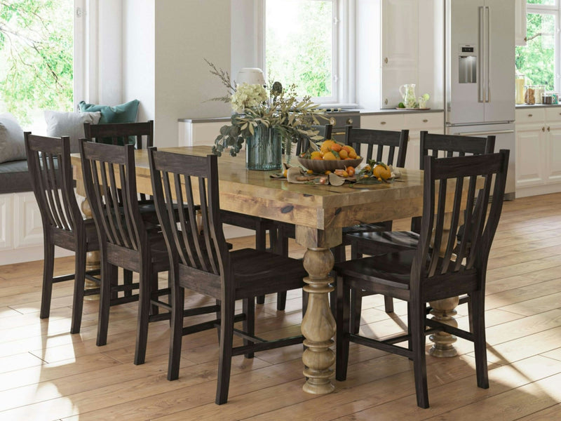 In a bright, spacious kitchen, the Annli Dining Table in Harvest Wheat by James+James is paired with six dark wooden chairs. The table is adorned with a floral arrangement and a tray of oranges. Sunlight streams through large windows, illuminating the light wood flooring and white cabinetry.